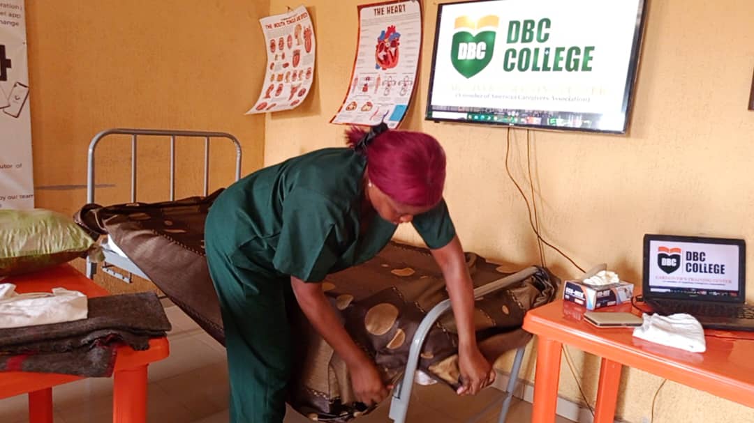 Practical training at DBC College: a learner preparing a patient bed beside teaching charts